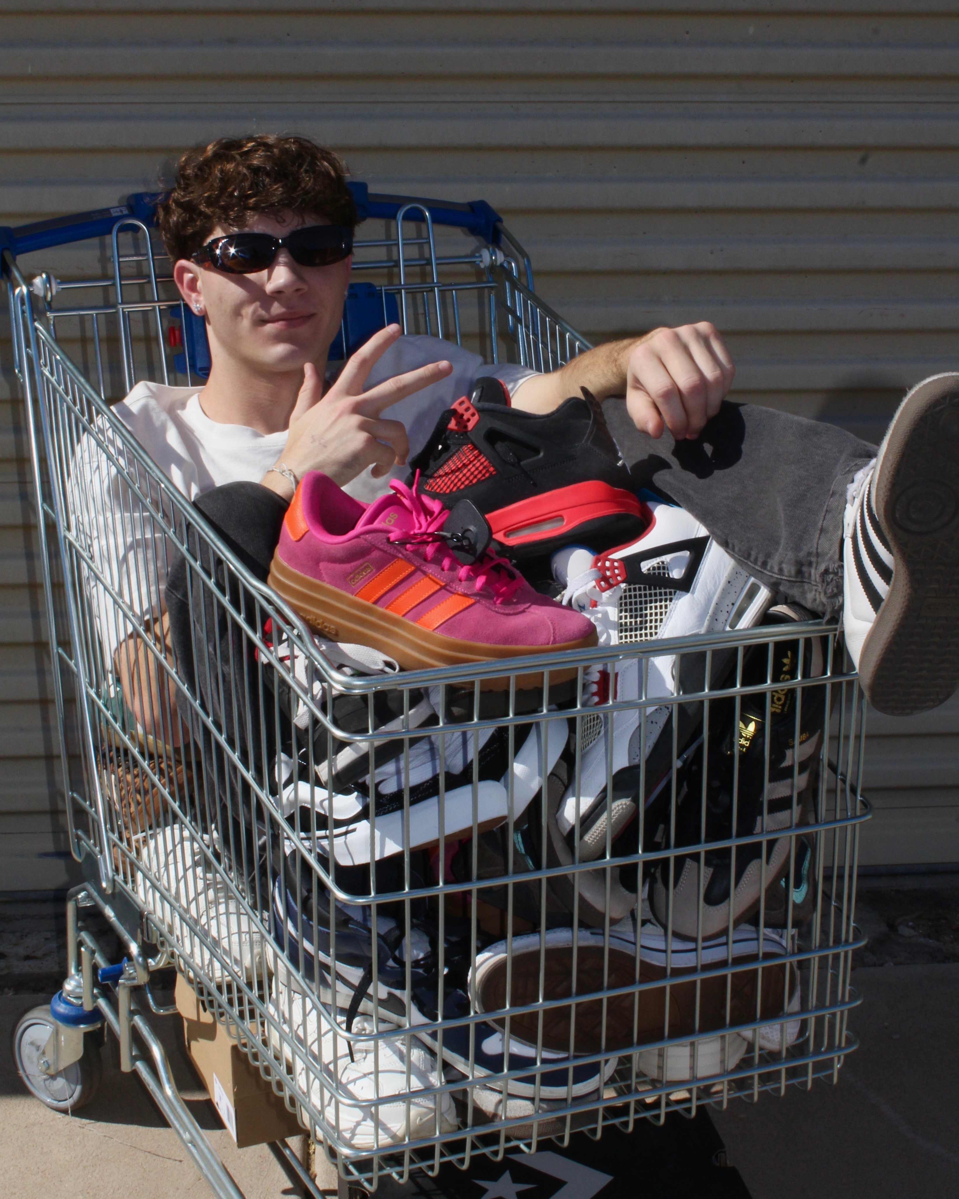 boy posing in shopping cart filled with sneakers